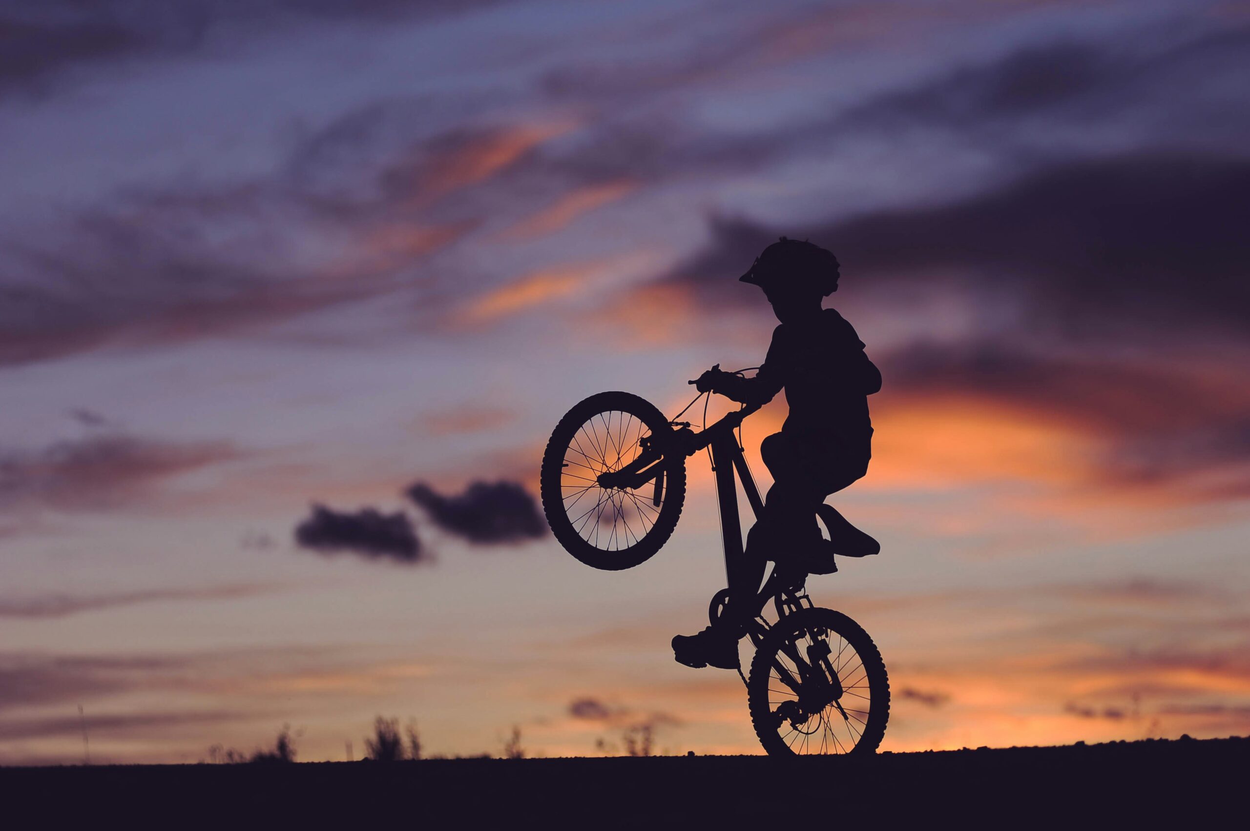 Silhouette of a child doing a wheelie on a bike at sunset, finding joy and freedom in the moment