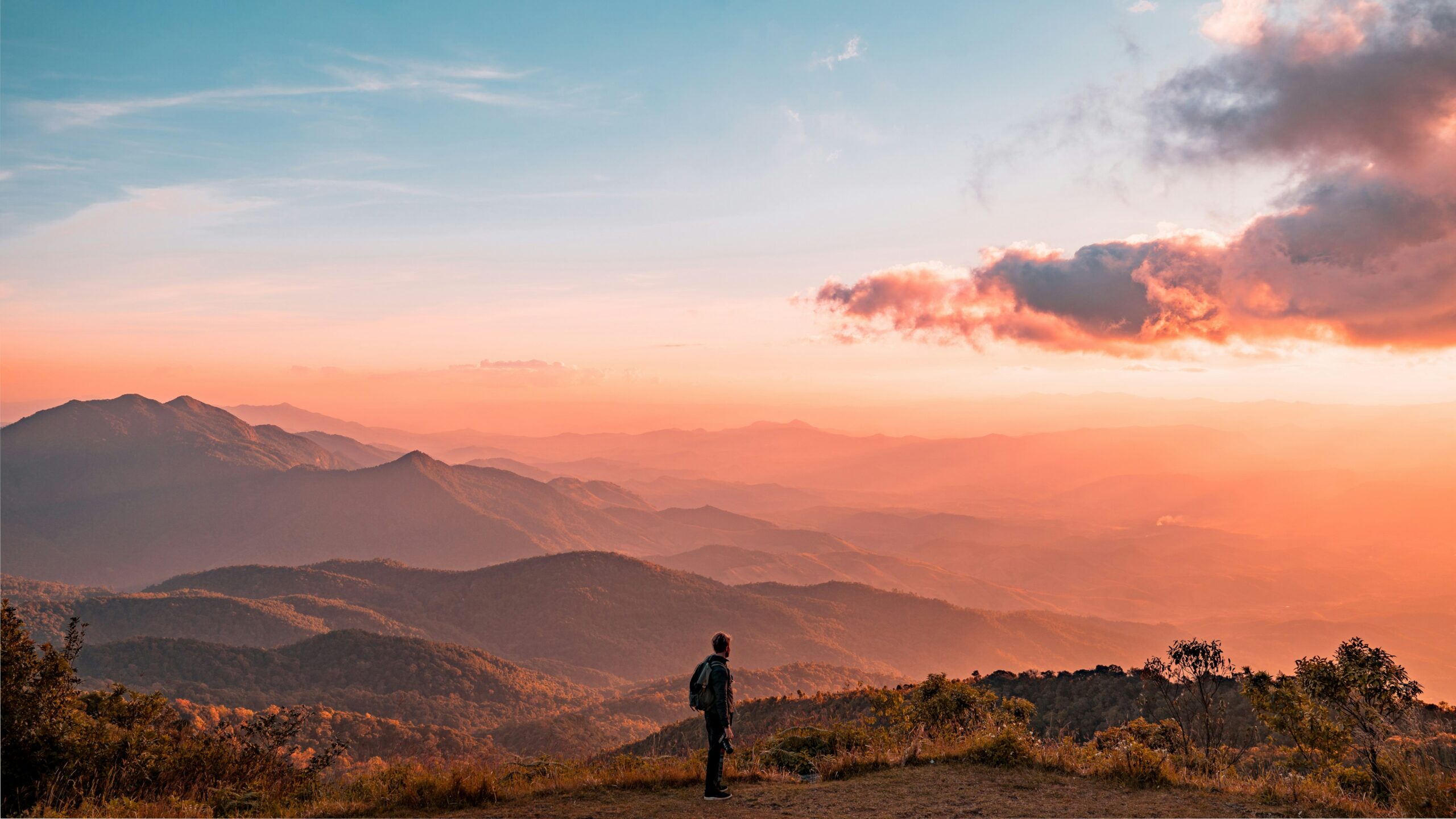 Person on a mountain peak at sunset, contemplating a beautiful view, reaching new heights in self-care