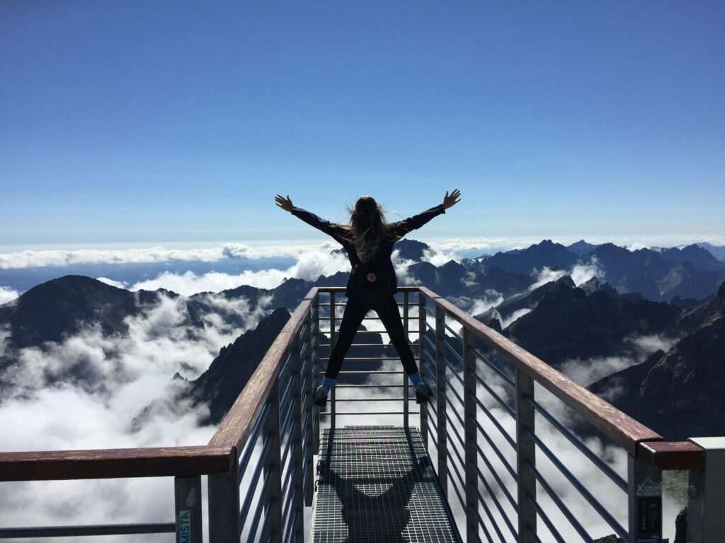A person with arms raised in victory on a high mountain peak, representing a feeling of confidence and success after surviving bullying.